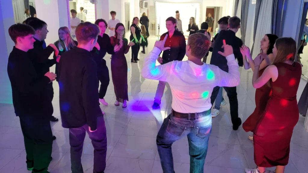 Młodzież tańczy w grupie na środku sali podczas 18-stki przy klubowym oświetleniu.